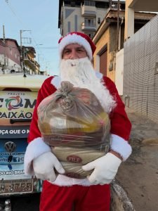 Homem vestido de papai noel segurando cesta básica para distribuição
